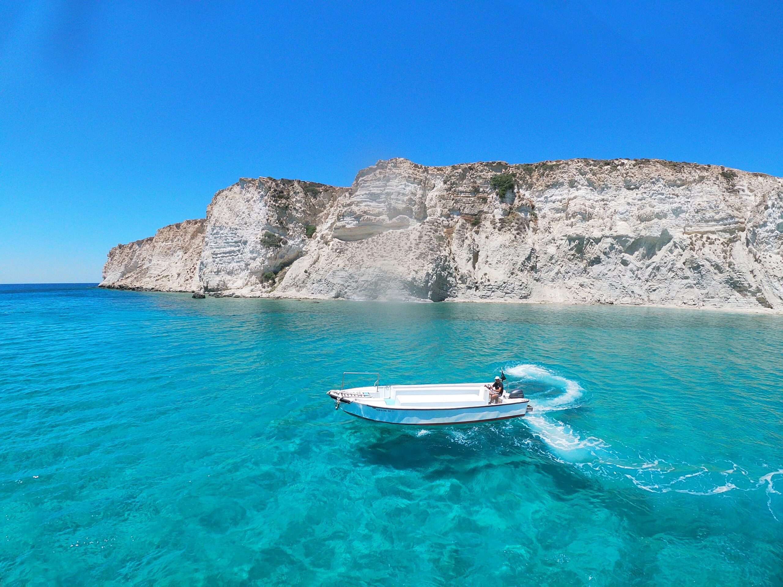 crystal blue waters with a small sail boat by rock formation in Crete