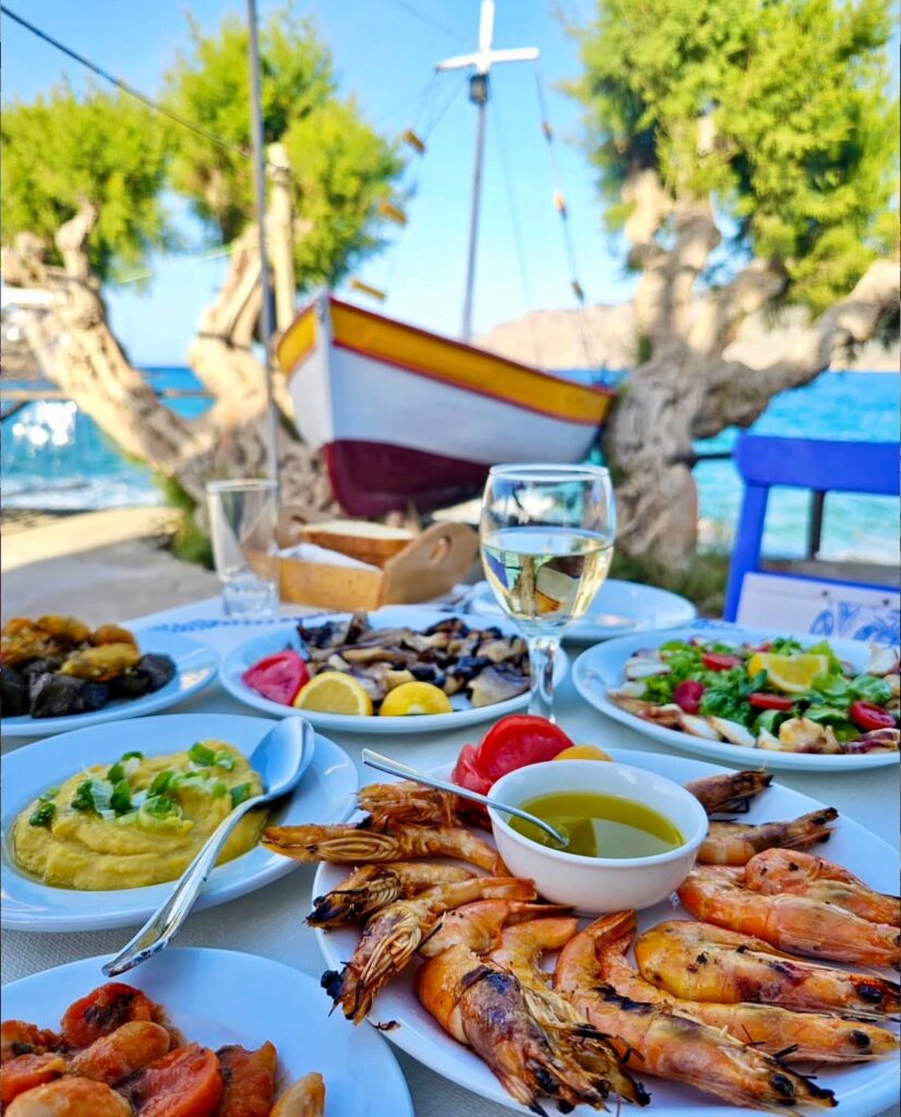 table of food at cretan restaurants with a glass os wine, boat and seaview